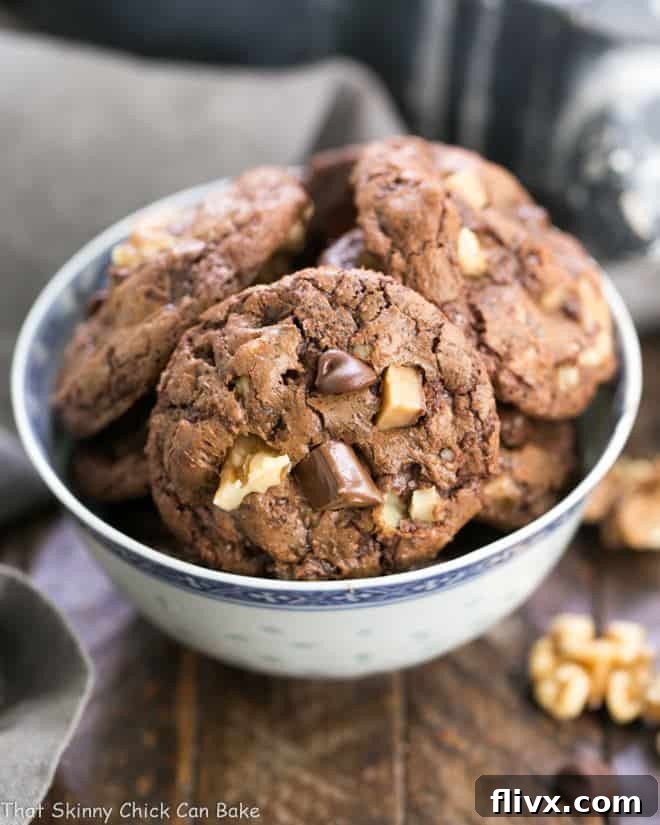 A close-up shot of delicious Chocolate Toffee Cookies piled high in a white and blue bowl, showcasing their rich chocolate color and visible toffee and walnut pieces.