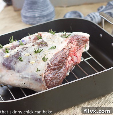 A roasted glazed leg of lamb with garlic and rosemary, shown in a roasting pan before carving.