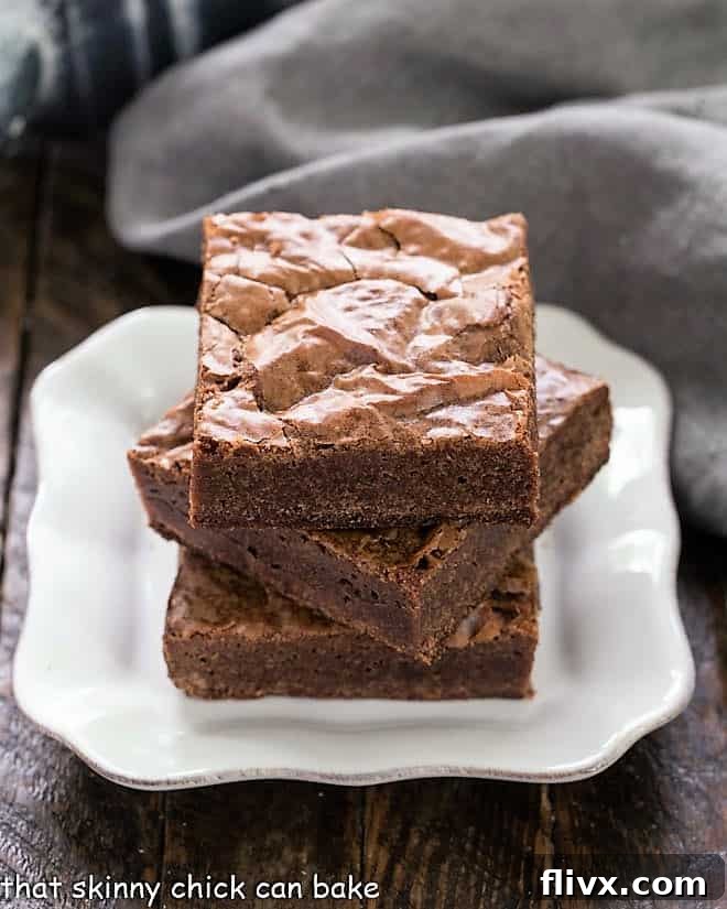 A tempting stack of perfectly cut Homemade Fudgy Brownies on a small white plate, highlighting their moist, dense interior and signature crackly top.