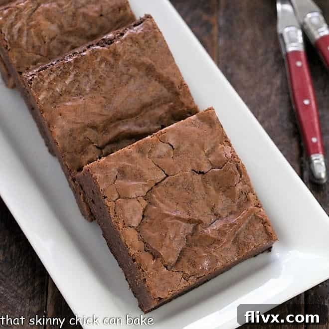 A close-up view of intensely fudgy brownies on a pristine white tray, showcasing their moist interior, rich chocolate hue, and inviting texture, ready to be enjoyed.