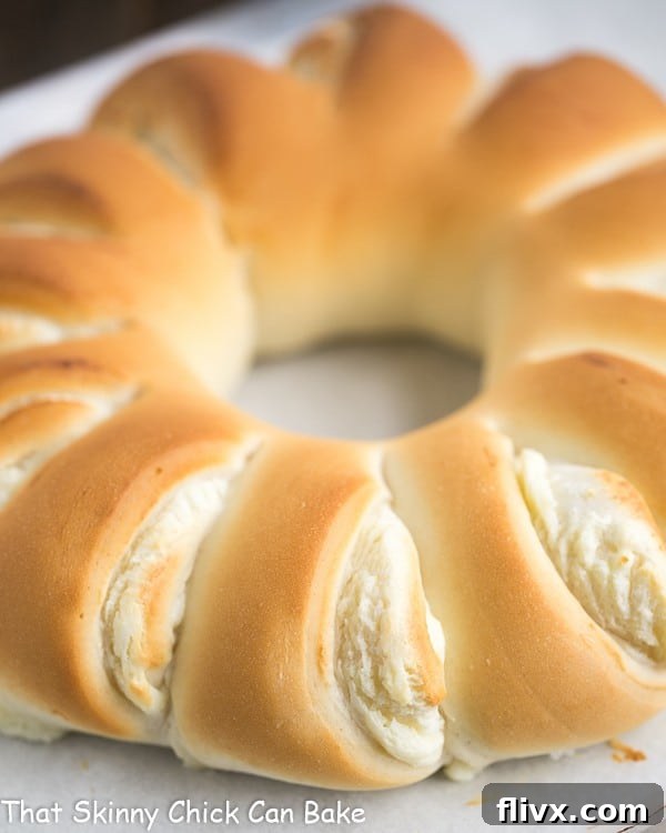 Close-up view of a Cream Cheese Tea Roll, perfectly baked to a golden hue, resting on a parchment-lined baking sheet, showcasing its alluring filling.