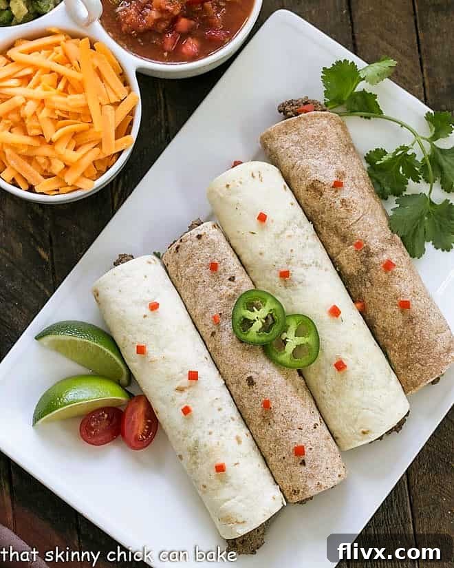 Overhead view of 4 soft shell beef tacos on a white platter with peppers and cilantro to garnish, beautifully arranged.
