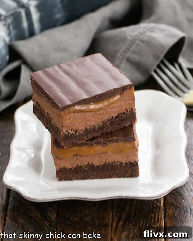 A tantalizing stack of two Milky Way Brownies, perfectly cut to reveal their distinct chocolate, nougat, and caramel layers, resting on a clean white plate.