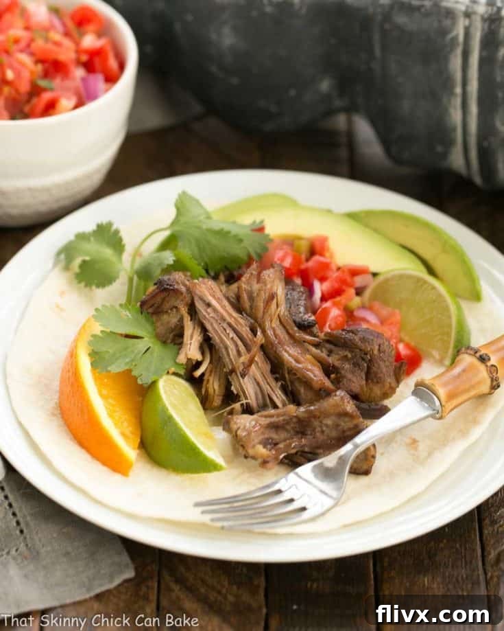 Slow cooked Pork Carnitas over a tortilla on a white plate, ready to be enjoyed.