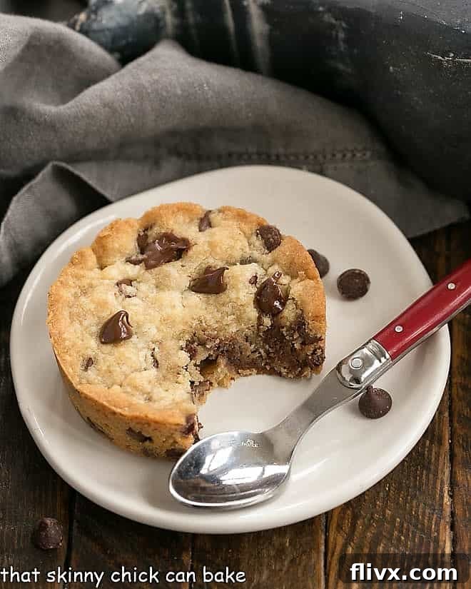 Round chocolate chip cookie bar with a few bites removed on a round white plate with a red handled spoon.