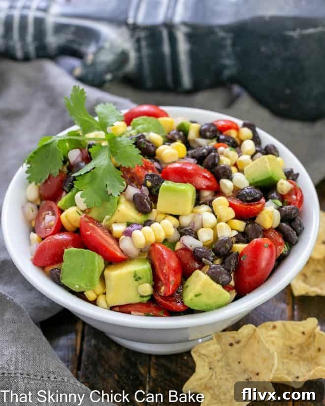 White serving bowl of corn salsa with a few scoops corn chips to the side