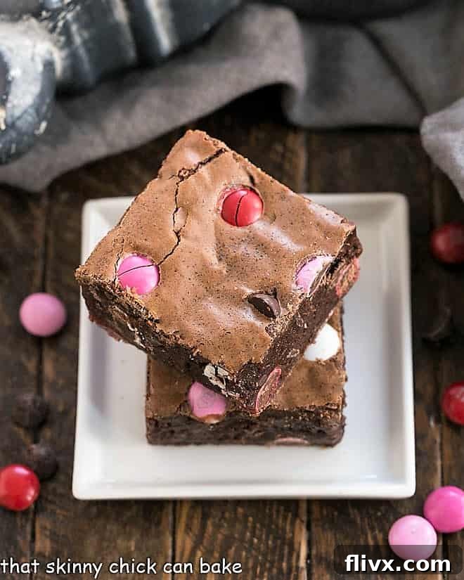 Two homemade brownies with M&M's stacked on a small square white plate