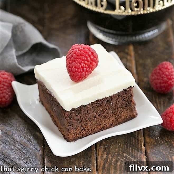 A raspberry brownie topped with cream cheese frosting and a fresh raspberry on a white plate.