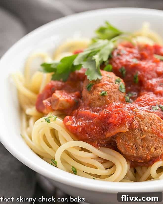 Close-up view of a hearty homemade pasta sauce with rich sausage pieces, served over perfectly cooked spaghetti in a white bowl, garnished with fresh herbs.