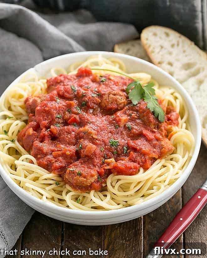 A beautiful bowl of spaghetti generously topped with homemade sausage pasta sauce, accompanied by two slices of crusty bread and a fork, inviting you to dig in.