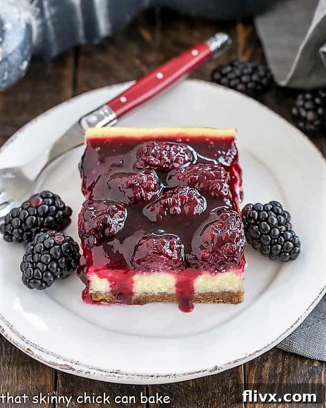 Delicious Blackberry Cheesecake Bars arranged on a round white plate, garnished with fresh blackberries and a red-handled fork, ready to be enjoyed.