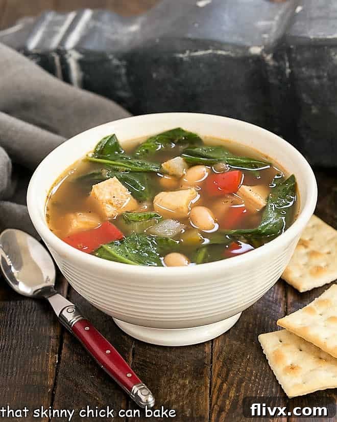 Small white bowl of white chicken chili with saltine crackers and a red handled spoon, ready to eat