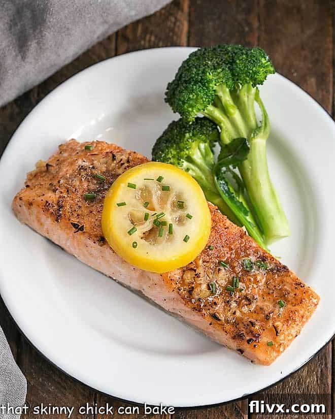 Overhead view of a perfectly roasted salmon fillet topped with a vibrant lemon slice, resting on a white plate alongside fresh green broccoli florets. The rich glaze is visible, hinting at the delicious flavors within.