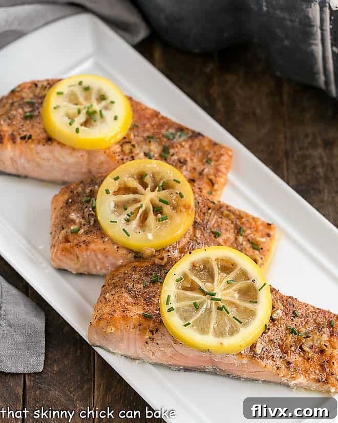 Three beautifully roasted salmon fillets, each adorned with a fresh lemon slice, artfully arranged on a pristine white serving tray, ready to be enjoyed.