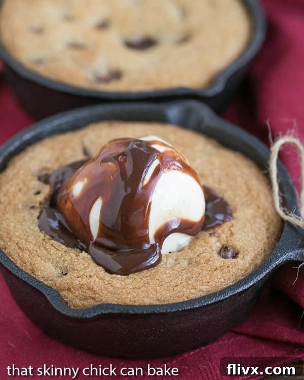 Close up of a warm Skillet Chocolate Chip Cookie, perfectly baked, topped with a scoop of vanilla ice cream and drizzled with chocolate fudge sauce