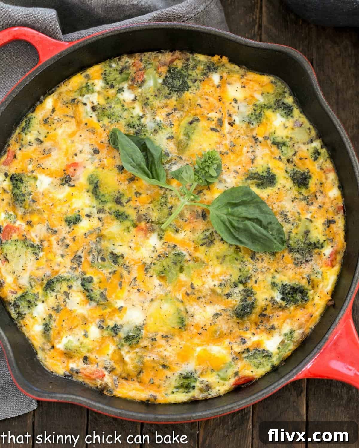 Overhead view of roasted broccoli frittata in a red cast iron pan, showing a generous slice removed.