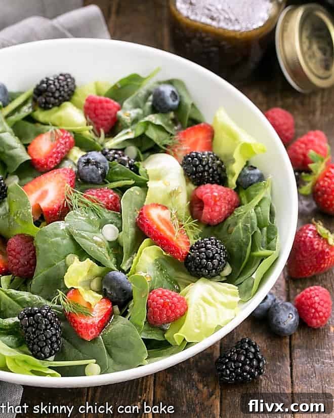 Spinach berry salad in a white ceramic bowl surrounded by fresh berries