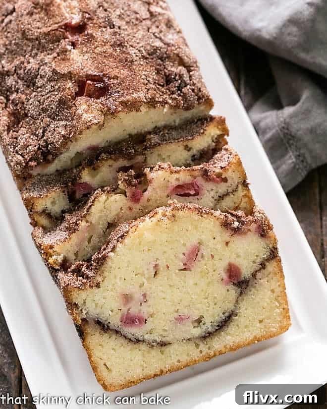A golden-brown loaf of Cinnamon Swirl Rhubarb Bread on a pristine white platter, showcasing its moist texture and subtle cinnamon swirl.