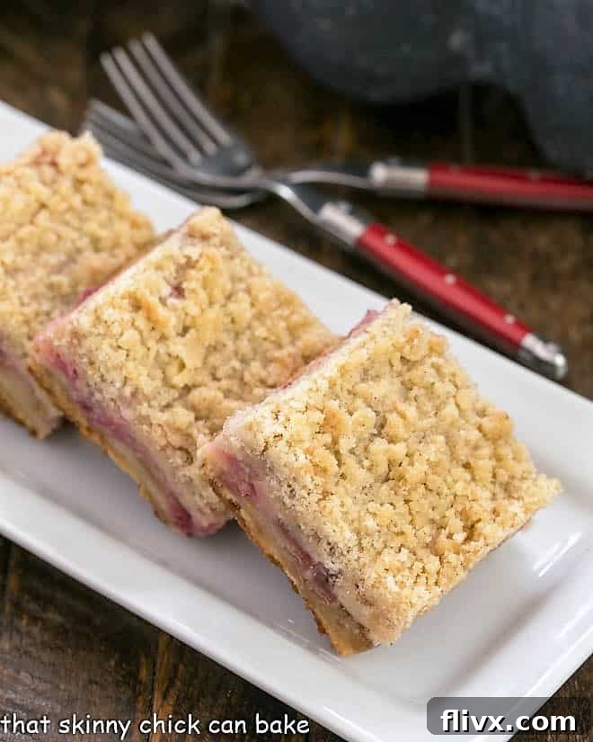 Luscious Rhubarb Bars with a shortbread crust, sweet and tart rhubarb filling and a streusel topping Three-layered Streusel Topped Rhubarb Bars artfully arranged on a pristine white tray, showcasing the golden shortbread crust, vibrant pink filling, and a generous crumbly topping.