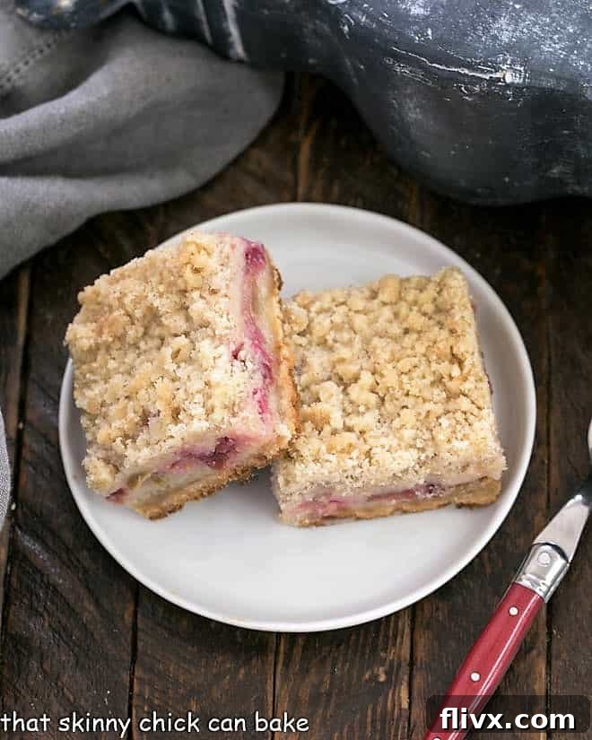 Rhubarb Crumble Bars 2 Two golden-brown Streusel Topped Rhubarb Bars, showcasing their distinct layers and crumbly texture, resting on a pristine round white plate.