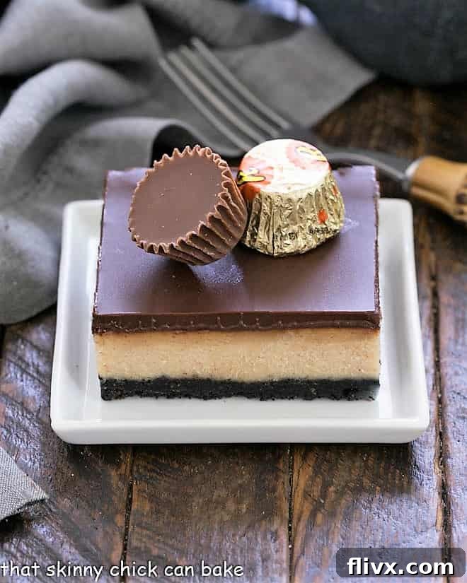 Close-up of a layered peanut butter cheesecake bar topped with two mini peanut butter cups, showing the creamy texture.