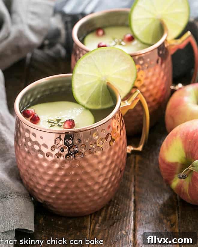 Two glistening copper mugs filled with Apple Cider Moscow Mules, garnished with crisp apple slices and fresh lime wedges, sitting on a rustic wooden surface, evoking a cozy autumn atmosphere.