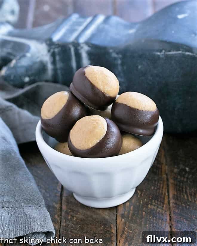A close-up shot of perfectly formed Chocolate Peanut Butter Balls, known as Buckeyes, nestled in a pristine white bowl. Each sphere boasts a smooth, half-dipped chocolate coating, revealing the rich peanut butter core, enticing viewers to indulge in this classic, easy-to-make dessert.