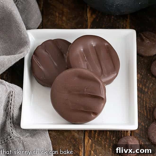 Overhead view of three freshly made peppermint patties on a square white plate, showcasing their perfect chocolate coating and classic shape.