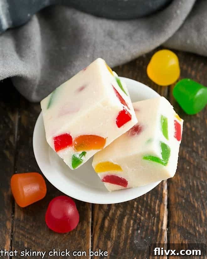 Two squares of vibrant white chocolate fudge in a small white bowl, showing colorful gumdrop pieces.
