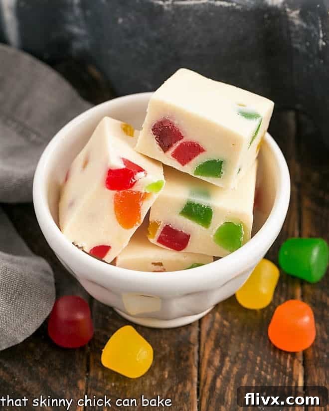 Small white bowl of vibrant stained glass white chocolate fudge with scattered gum drops, ready to enjoy.