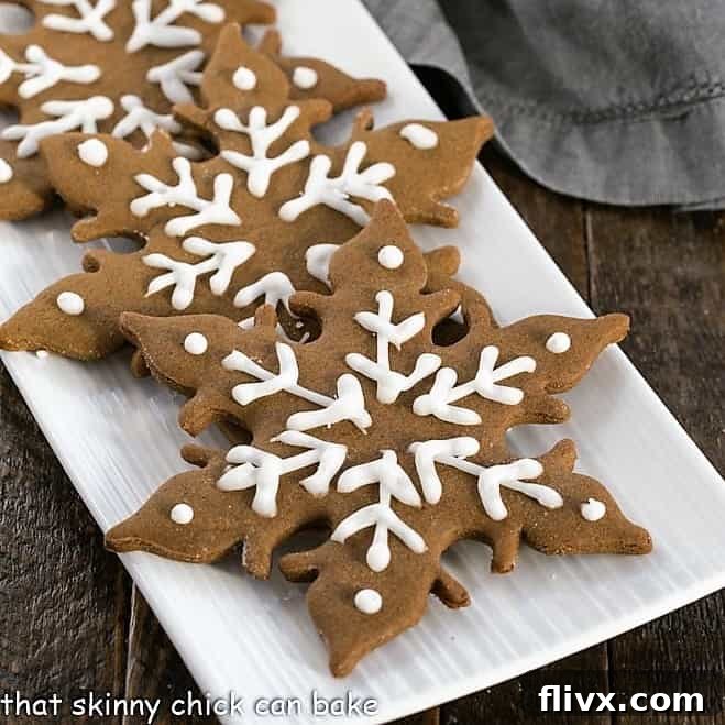 Beautifully decorated snowflake-shaped gingerbread cookies arranged on a white serving tray, ready for the holidays.