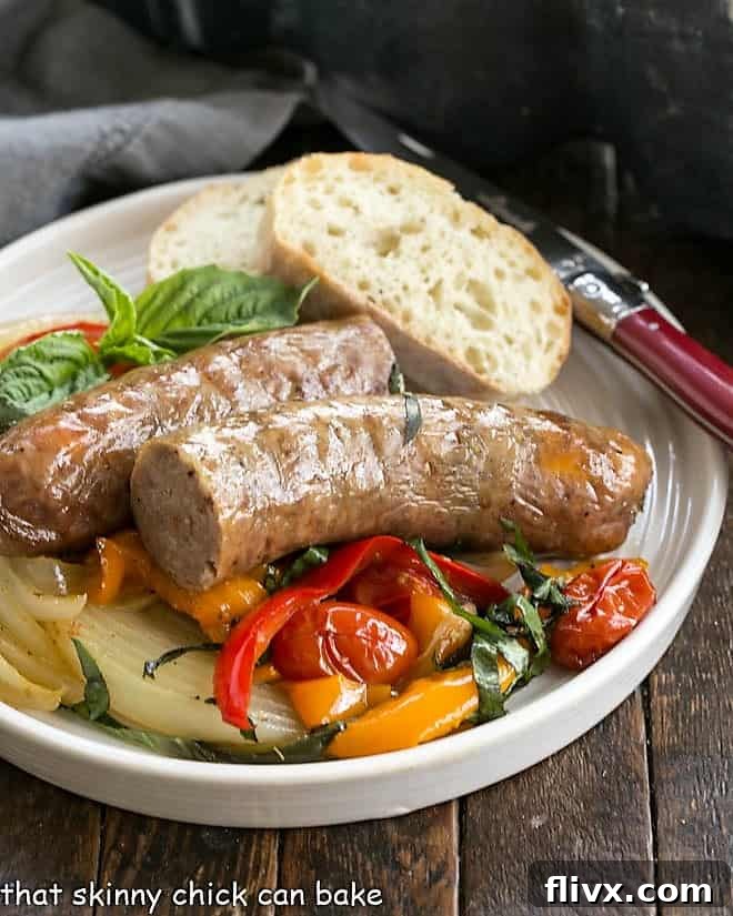 Sheet Pan Sausage and peppers served on a white dinner plate with a slice of rustic bread and a red handled fork