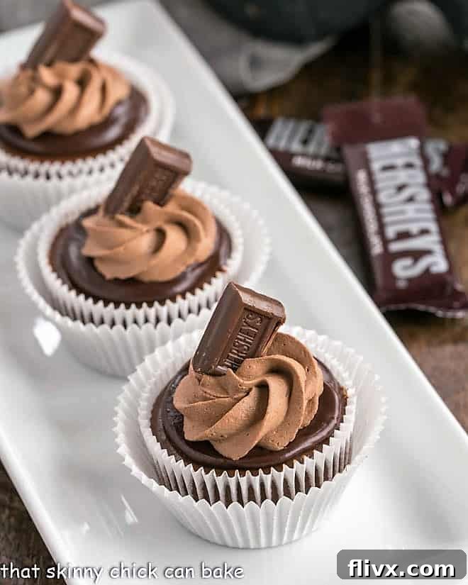 A white rectangular tray filled with an array of perfectly crafted mini chocolate cheesecakes, each topped with a swirl of chocolate whipped cream and a mini chocolate bar.