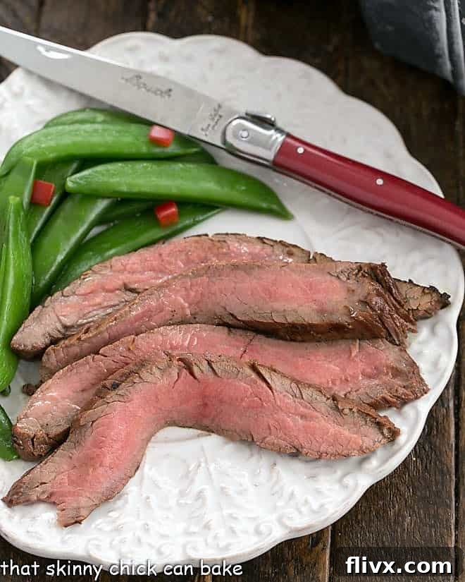 An overhead view of perfectly sliced flank steak, vibrant sugar snap peas, and a red-handled knife, showcasing the meal's appeal.