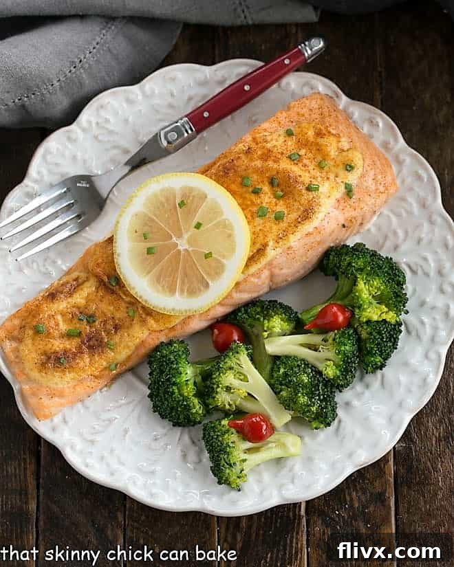 Overhead view of perfectly Oven Roasted Salmon topped with a fresh lemon slice, served on a white plate alongside vibrant green broccoli, ready for a healthy and quick dinner.