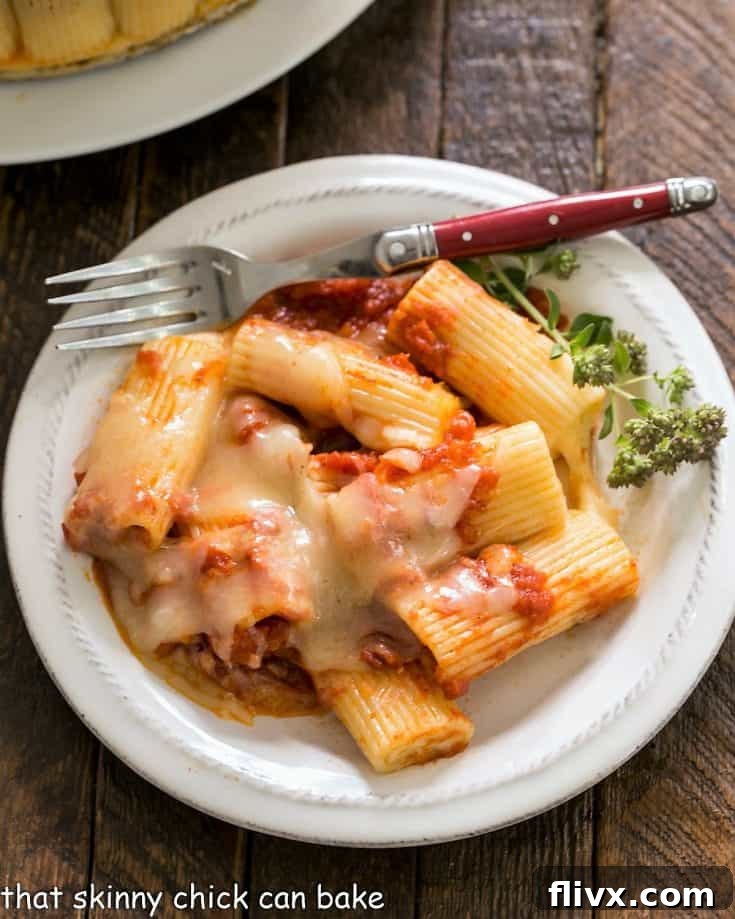 Overhead view of baked rigatoni on a small white plate with a fork and herb garnish