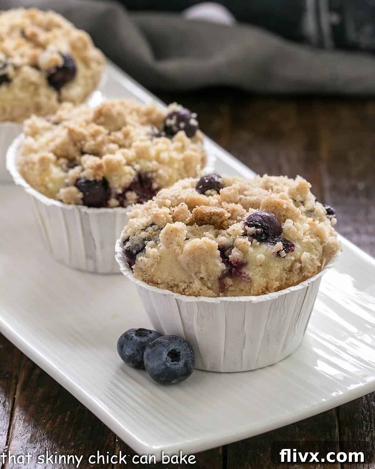 Blueberry Cream Cheese Muffins on a white ceramic tray, showcasing their golden tops and fresh blueberry garnish.