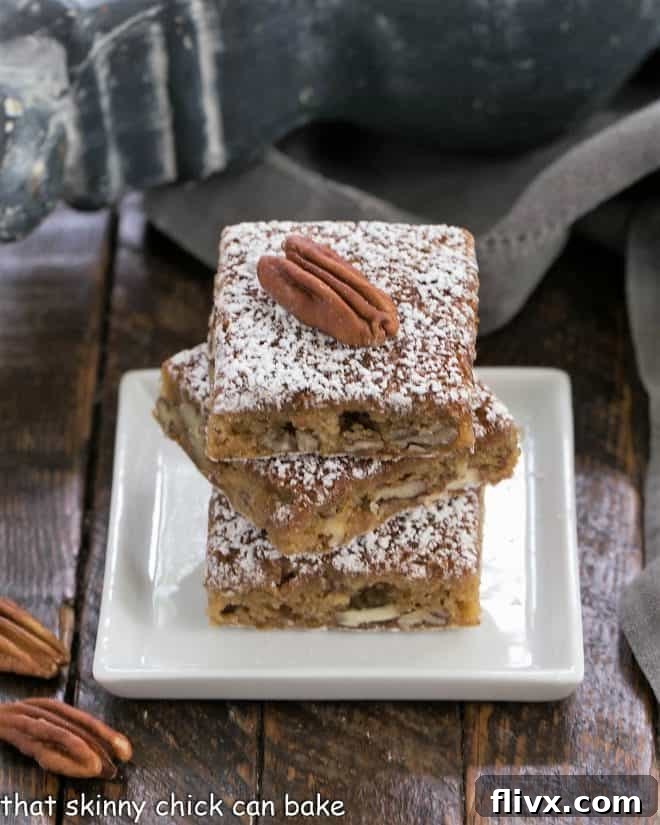 Three golden brown pecan bars, stacked delicately on a small square white plate, highlighting their inviting texture and toasted pecan topping.