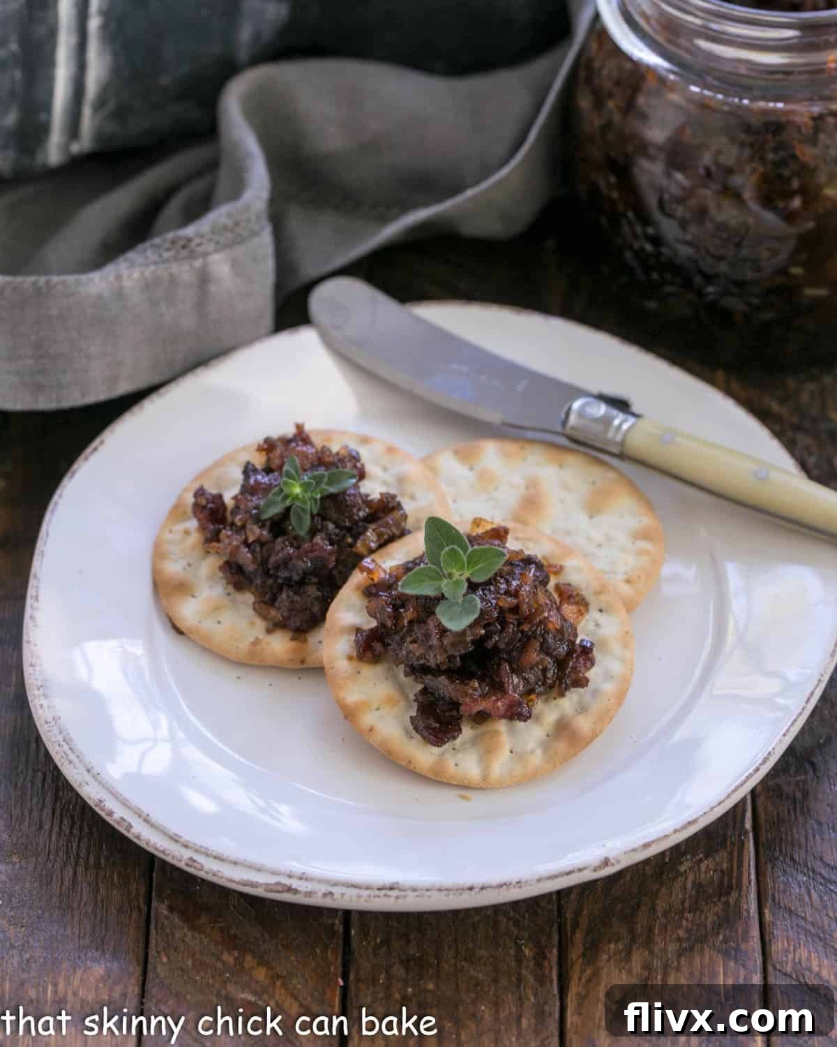 Bacon jam on crackers on a white appetizer plate, showcasing its rich texture and appetizing appeal.