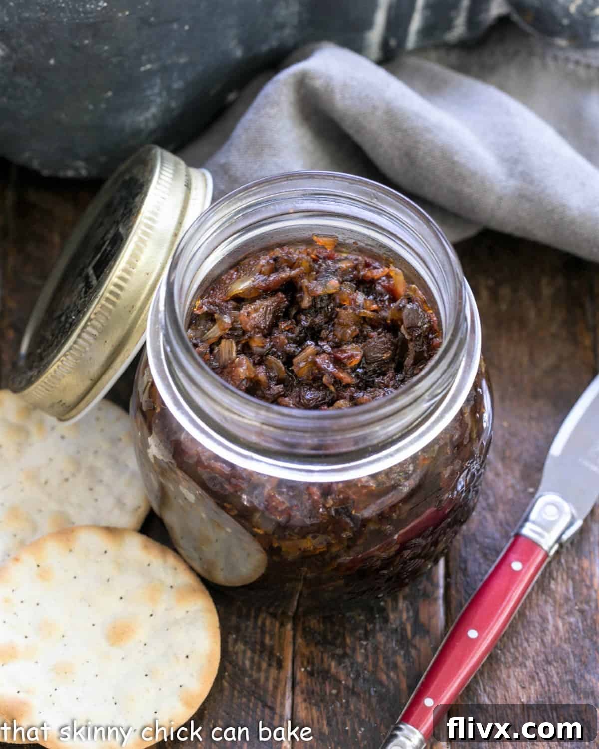 A jar of bacon jam with crackers and a red handled knife, suggesting elegant serving.