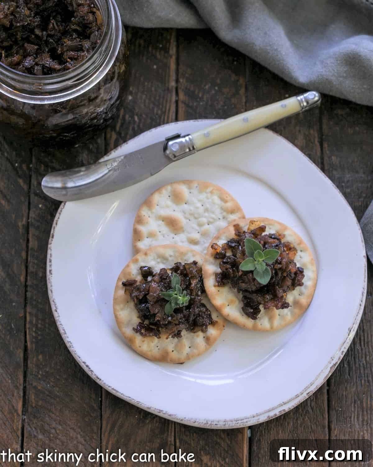 Overhead view of bacon jam on crackers with an ivory handle knife, emphasizing presentation.