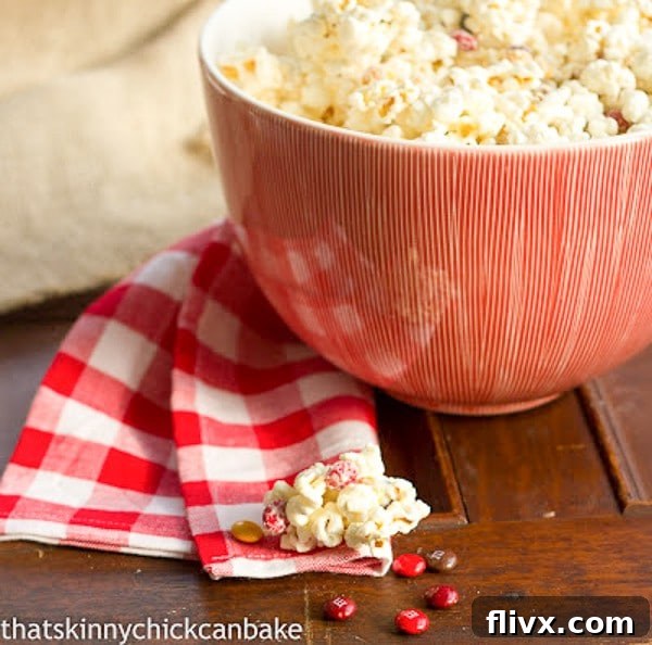 Delicious Holiday White Chocolate Popcorn served in a festive red bowl, accompanied by a charming red and white checked napkin.