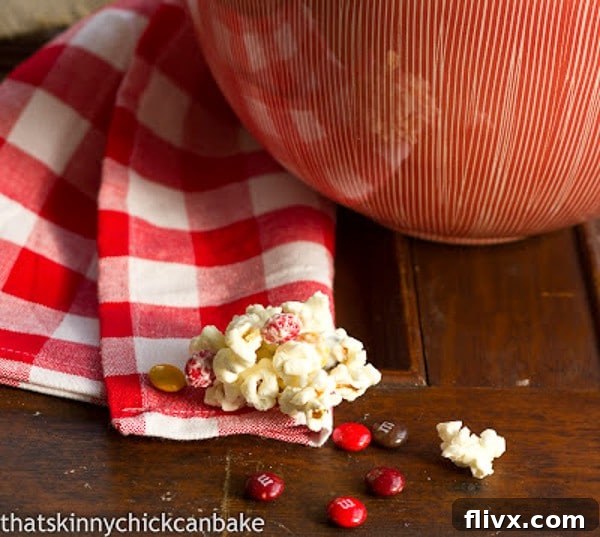 Festive White Chocolate Popcorn displayed in front of a serving bowl filled with colorful M&M's, highlighting its delicious candy additions.