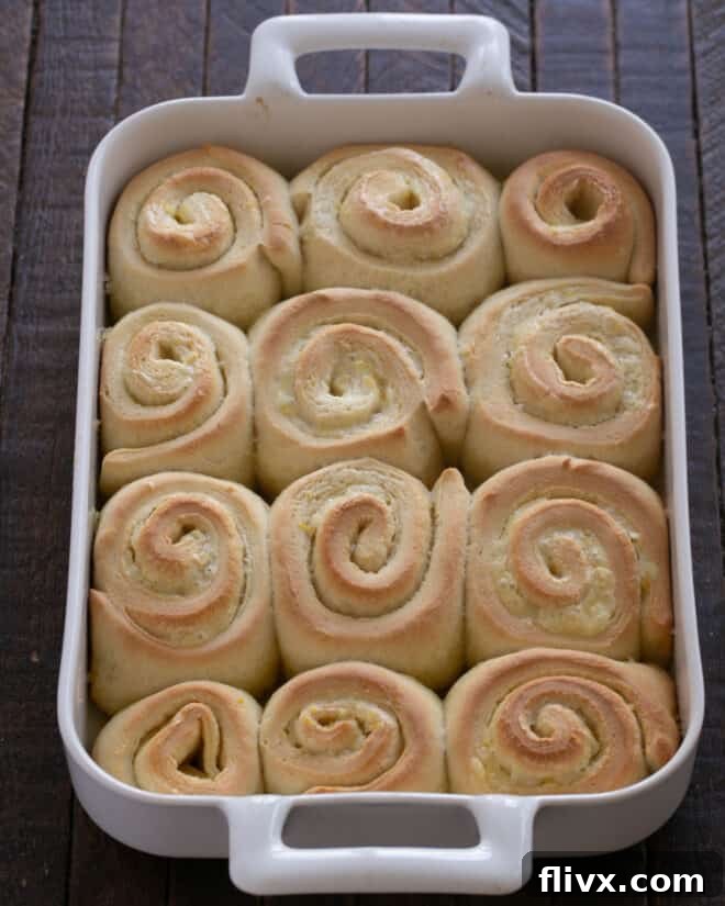 Fluffy Orange Glazed Rolls 17 Freshly baked orange rolls in the pan, golden brown, with the remaining orange frosting being spread over them while still warm.