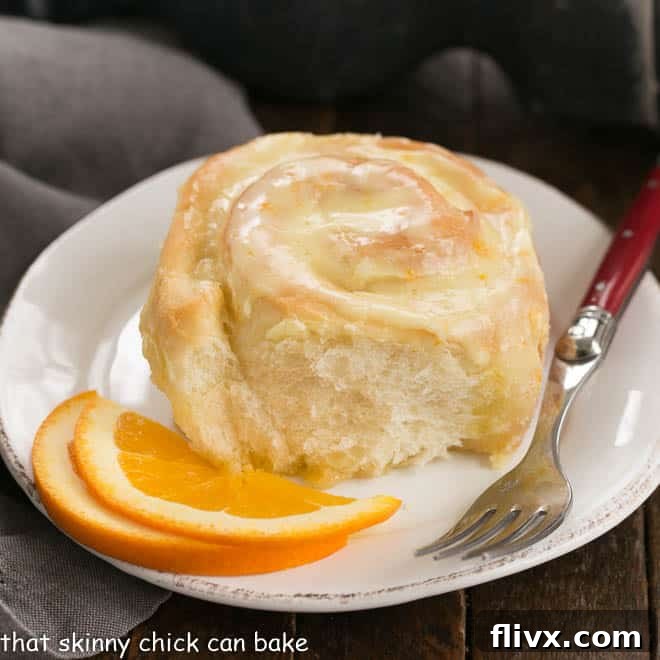 Orange Roll on a round white plate with two orange slices and a red handled fork