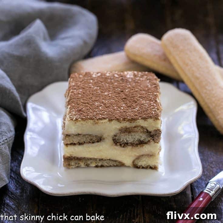 A slice of classic tiramisu on a square white plate with 2 ladyfingers