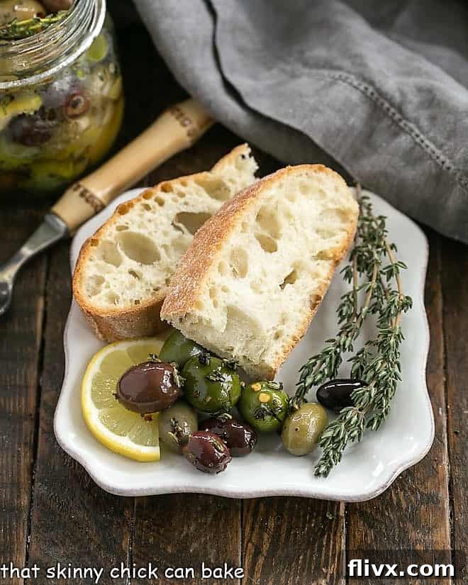 Herbed olives on a white plate with crusty bread and fresh thyme sprigs.