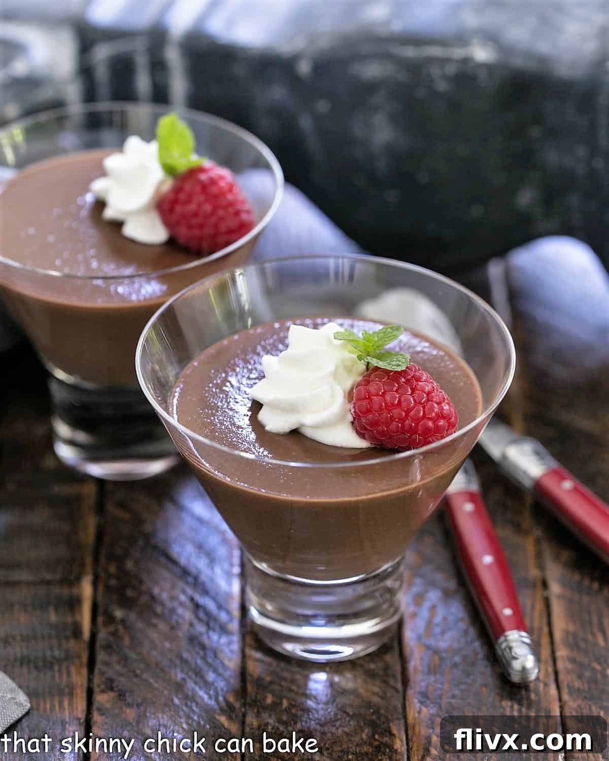 Two glass dishes filled with Italian chocolate pudding, elegantly topped with swirls of whipped cream, vibrant red raspberries, and a fresh sprig of mint, ready to be served as a sophisticated dessert.