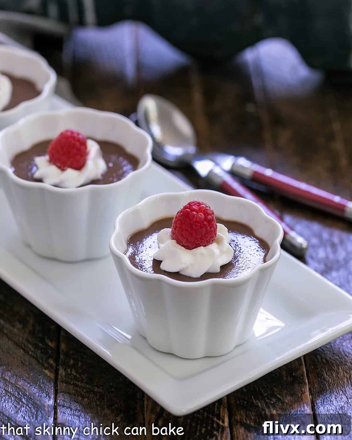Three servings of rich Italian chocolate pudding (Budino) in elegant white ramekins, each perfectly topped with a dollop of whipped cream and a fresh raspberry, highlighting its sophisticated presentation.