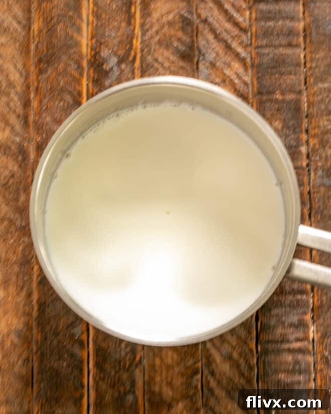 Milk and cream gently simmering in a saucepan on the stovetop, indicating the first step in preparing the chocolate pudding base.